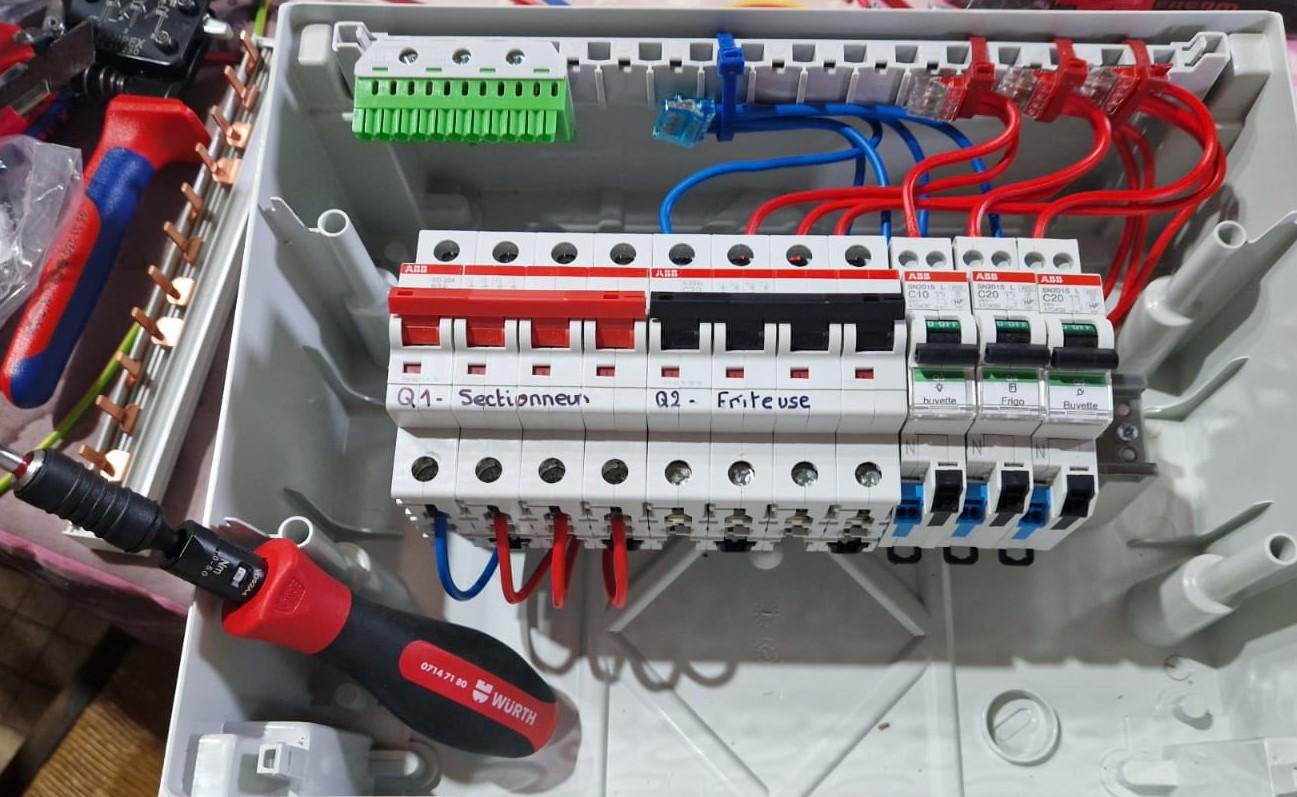 Électricien industriel réalisant le câblage d’un tableau électrique avec disjoncteurs et raccordements soignés